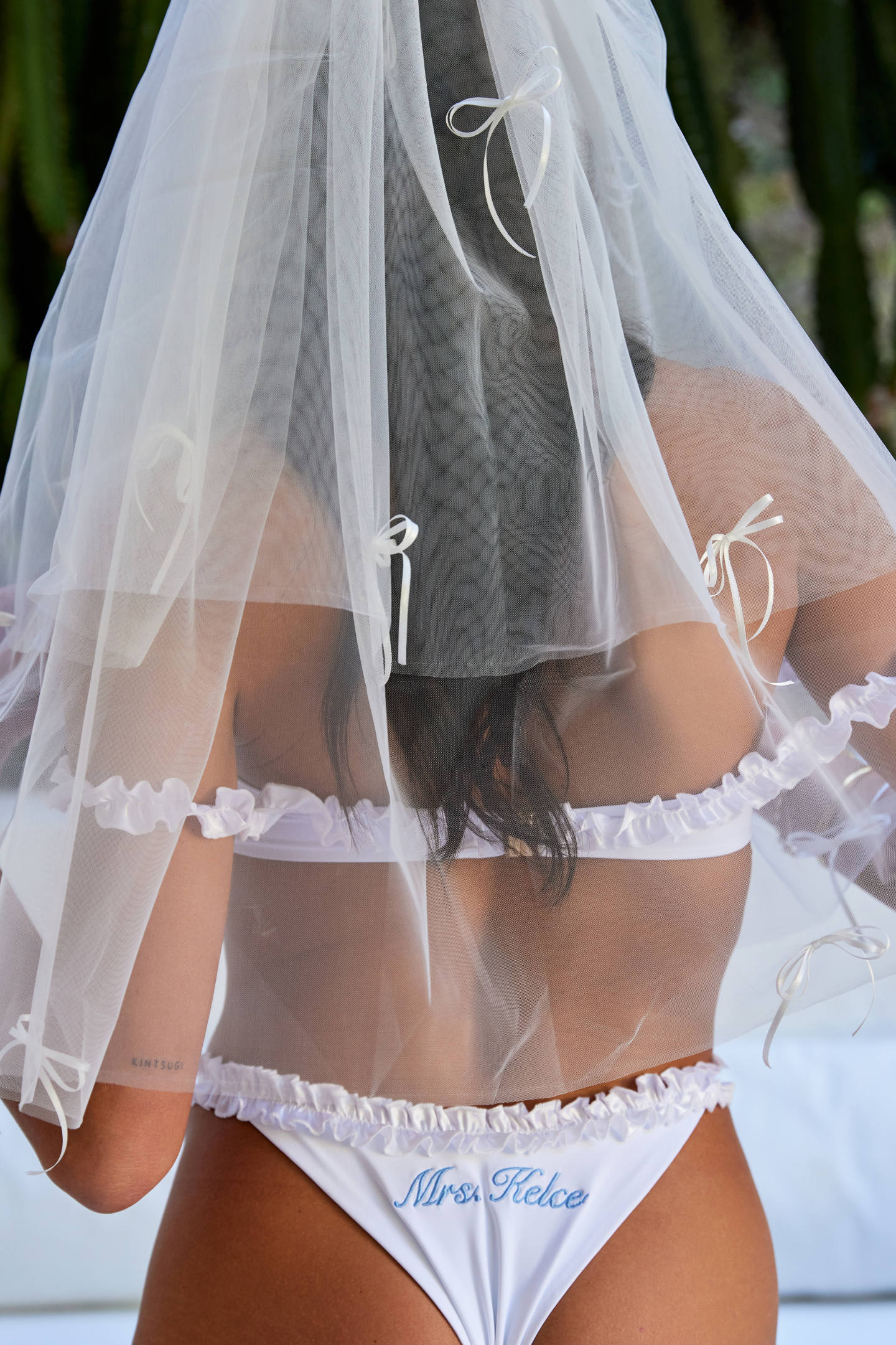 Woman wearing ALT’s Roma top, Margot bottom, Belle Bow veil. a white bridal bikini set, with cacti in the background. White tulle bridal veil with small bow details. Blue embroidery on bottoms Mrs. Kelce