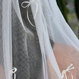 Woman wearing ALT’s Roma top, Margot bottom, Belle Bow veil. a white bridal bikini set, with cacti in the background. White tulle bridal veil with small bow details