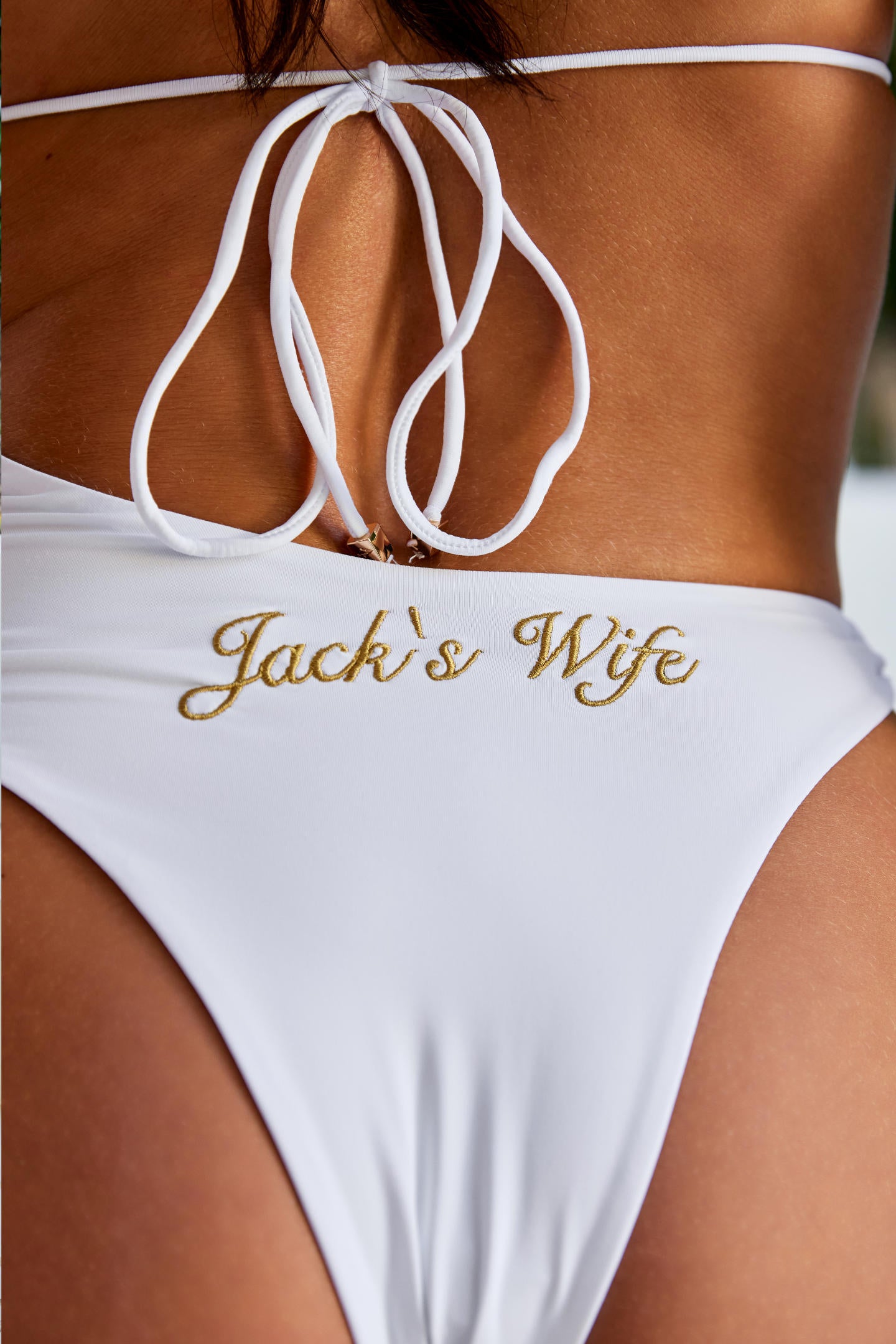Woman wearing ALT’s Elidy one piece, a white bridal one piece swimsuit with gold chain halter detailing, back tie and gold embroidery Jack's Wife