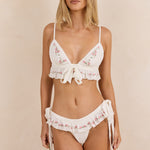 ALT's white Mimi brief shown from the front, floral ruffle trim beneath the matching bra, paired with a flower and stockings.