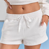 A close-up of the white Althea track short at the waist, a white drawstring tied in a bow over a double elasticated waistband and a side pocket.