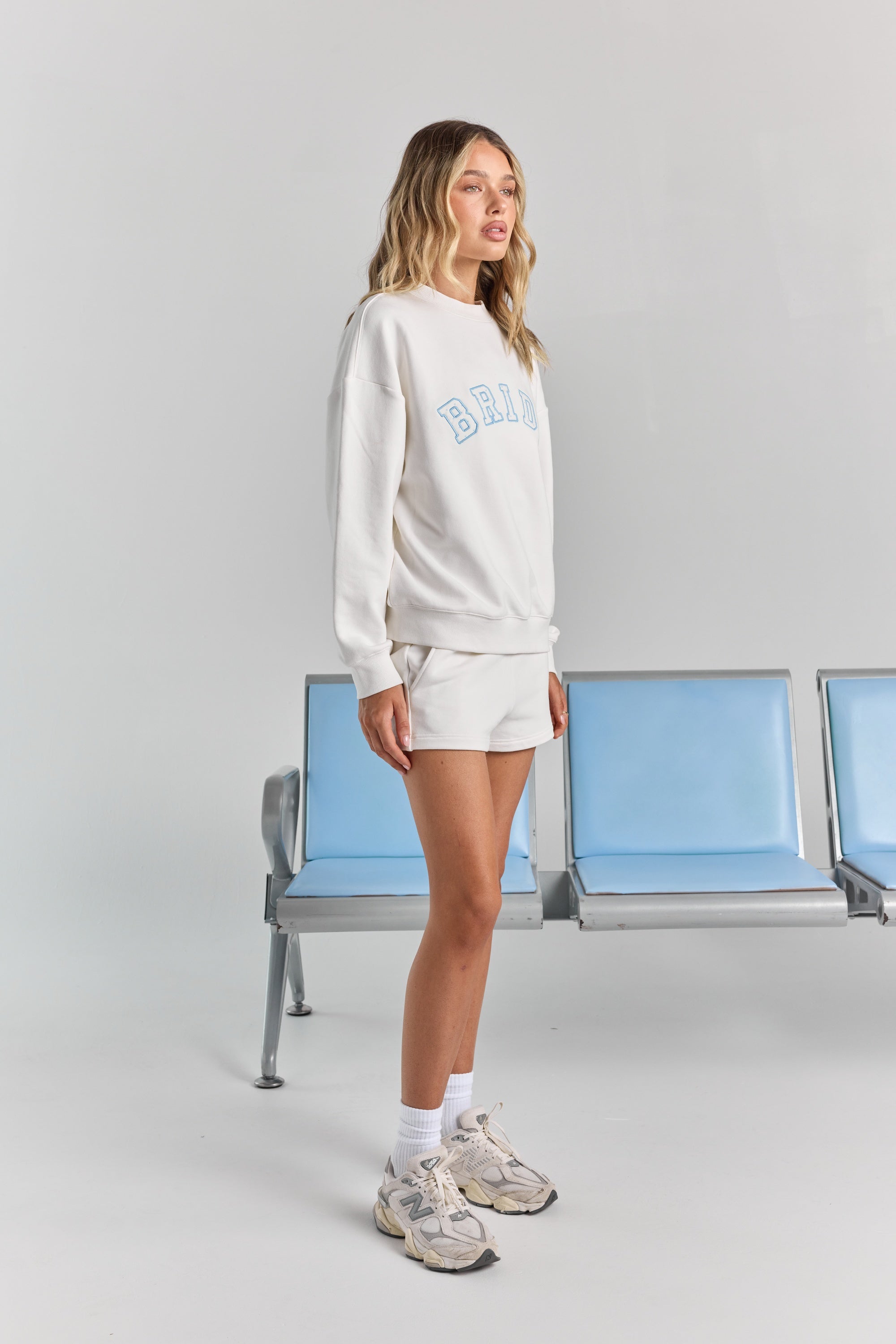 White Bride Althea track short from the side, showing the side seam pocket and short hem beneath the Bride Pia crew sweatshirt.