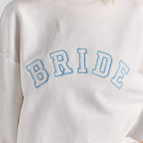 A close-up of BRIDE in heart-print varsity applique with a blue stitched outline across the chest of the white Bride Pia crew sweatshirt.