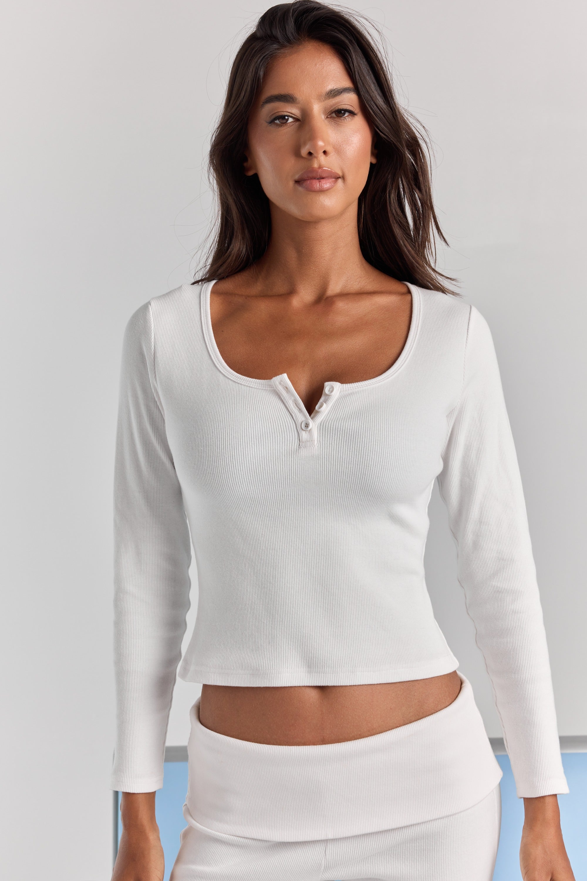 Closer front view of the white Cleo long sleeve top, with a wide scoop neck, short button placket and fitted ribbed sleeves.