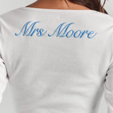 A close-up of personalized embroidery across the upper back of the white Cleo long sleeve top, just below the neckline.