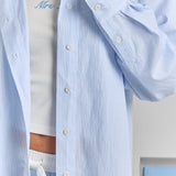 A close-up of the white buttons down the front placket and the buttoned cuff of the blue stripe Corinna button-up shirt, in a fine stripe.