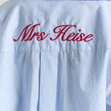 A close-up of personalized embroidery across the back yoke of the blue stripe Corinna button-up shirt, above the center box pleat.