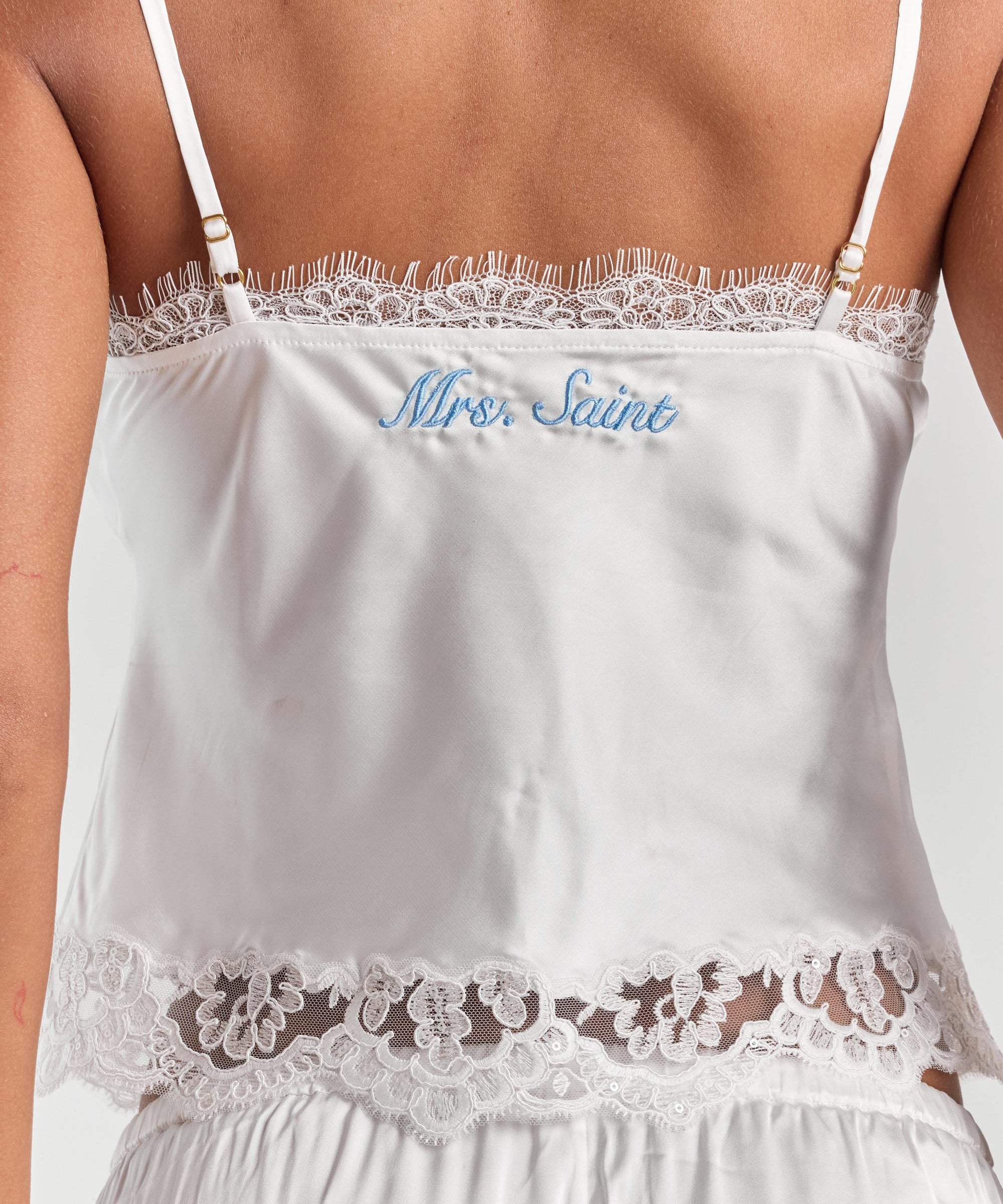 A close-up of personalized embroidery across the upper back of the white Eloise satin lace crop cami, below the eyelash lace.