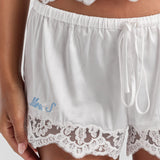 A close-up of the white Gianna satin lace short, with the drawstring tie, elasticated waist, floral lace hem and personalized embroidery at the leg.