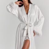 White Melita feather satin robe belted at the waist with its self-tie knotted in a bow, with a shawl collar and feather cuffs.