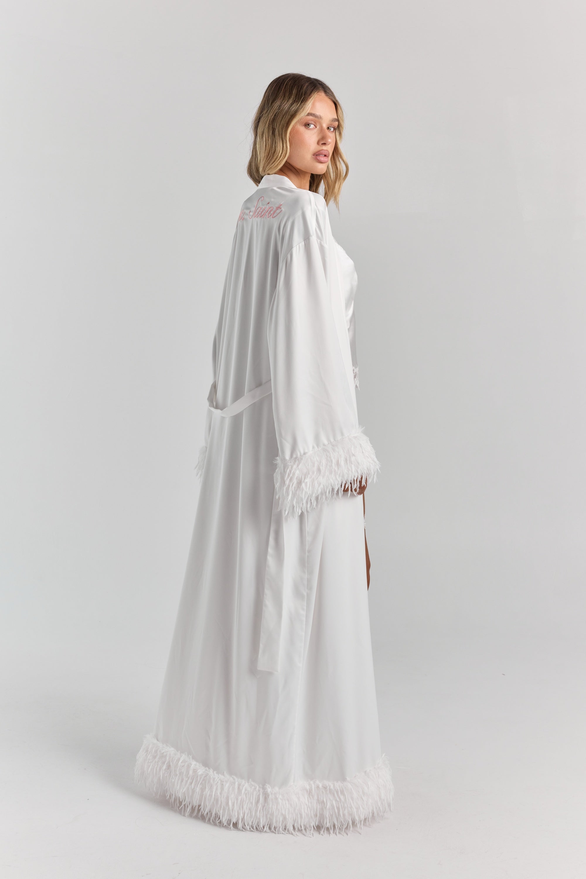 White Melita feather satin robe from a three-quarter back angle, with personalized embroidery at the upper back, the belt and a full feather hem.