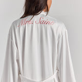 White Melita feather satin robe from behind, with personalized embroidery across the upper back, a self-tie belt and feather cuffs.