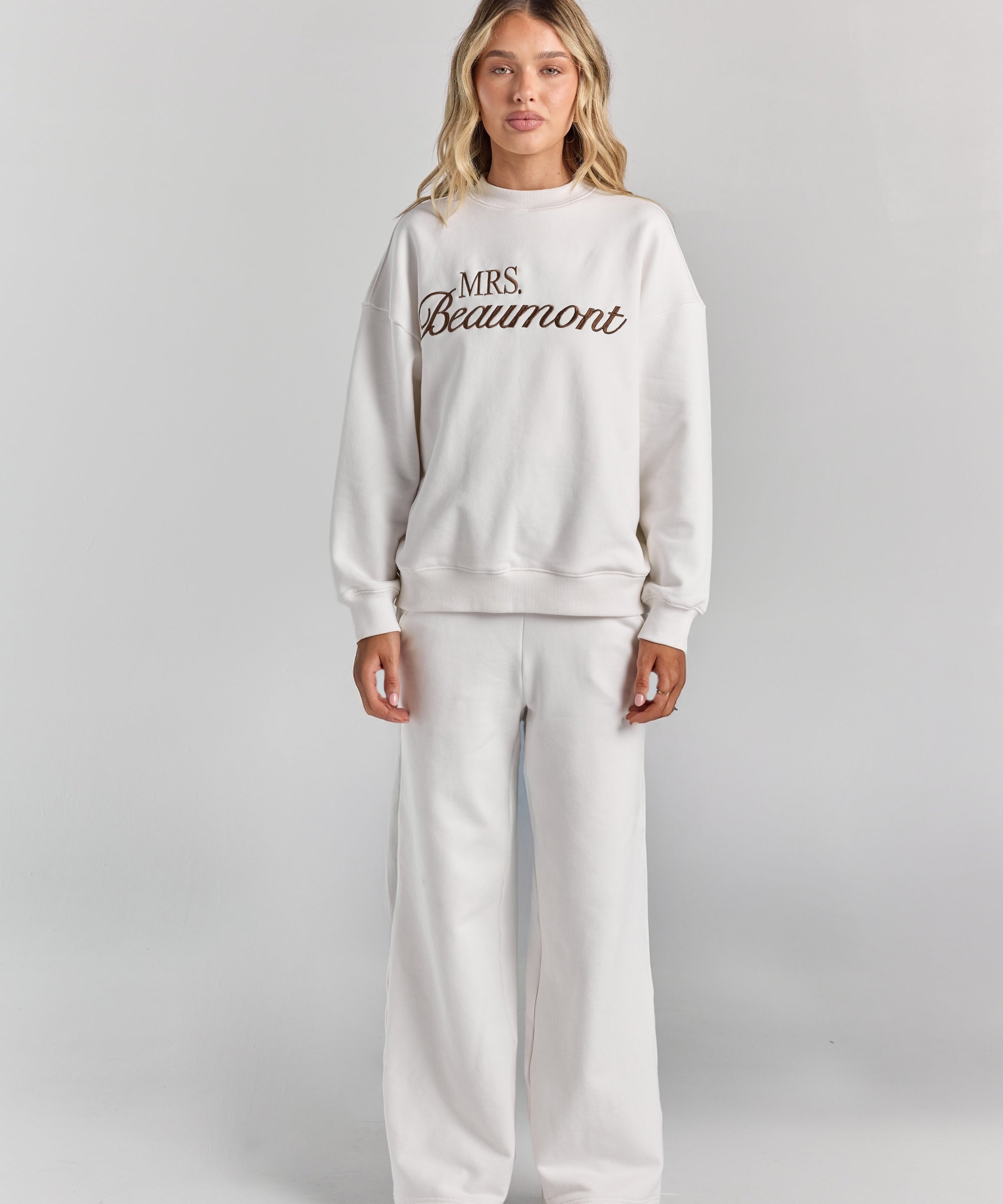 White Pia crew sweatshirt at full length, ending at the hip, with personalized embroidery across the chest, worn with the Paola trackpant.