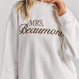 A close-up of personalized embroidery across the chest of the white Pia crew sweatshirt, between the ribbed neckline and ribbed hem.