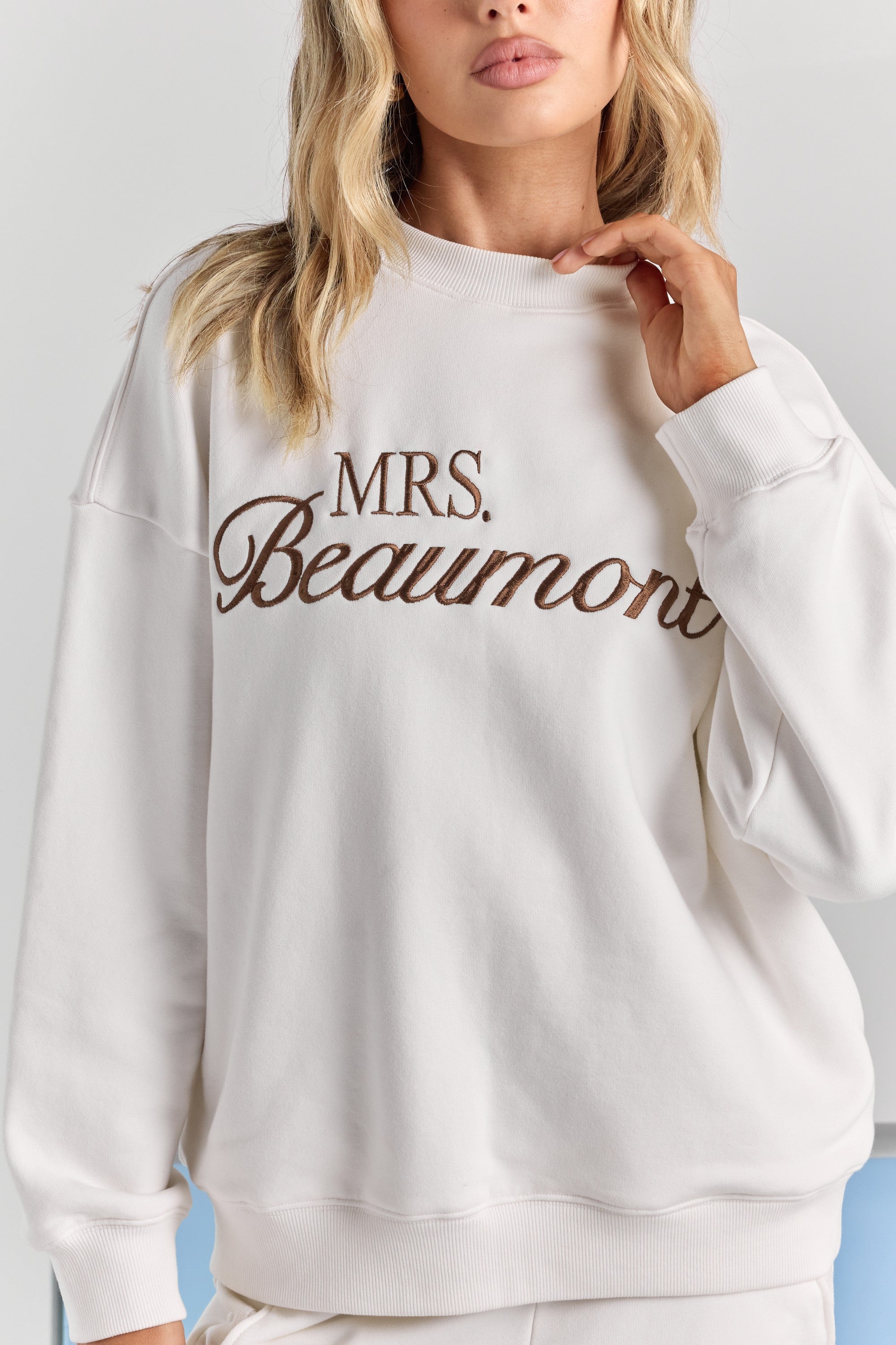 A close-up of personalized embroidery across the chest of the white Pia crew sweatshirt, between the ribbed neckline and ribbed hem.