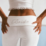 A close-up of the Bride rhinestone lettering across the fold-over waistband of ALT's white Rhinestone Frankie ribbed pant.