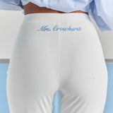 A close-up of personalized embroidery just below the back waistband of the white Vivienne travel pant, centered over the back seam.