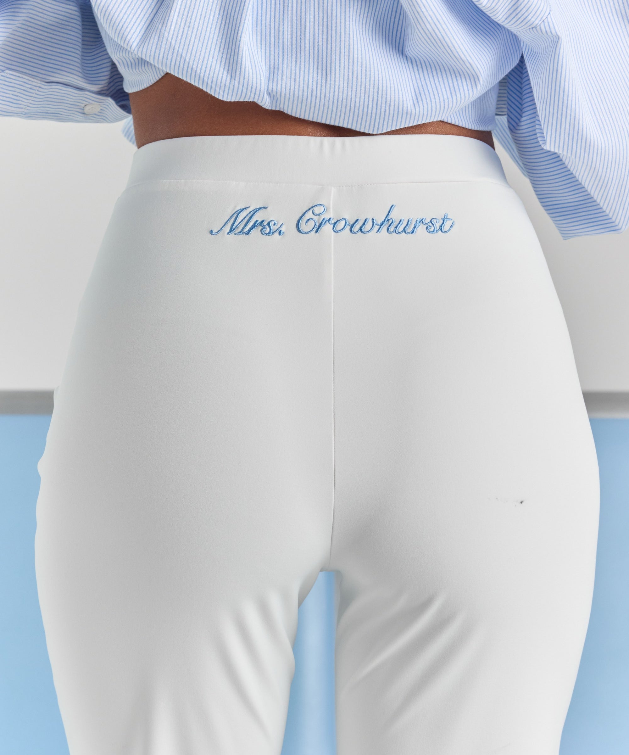 A close-up of personalized embroidery just below the back waistband of the white Vivienne travel pant, centered over the back seam.