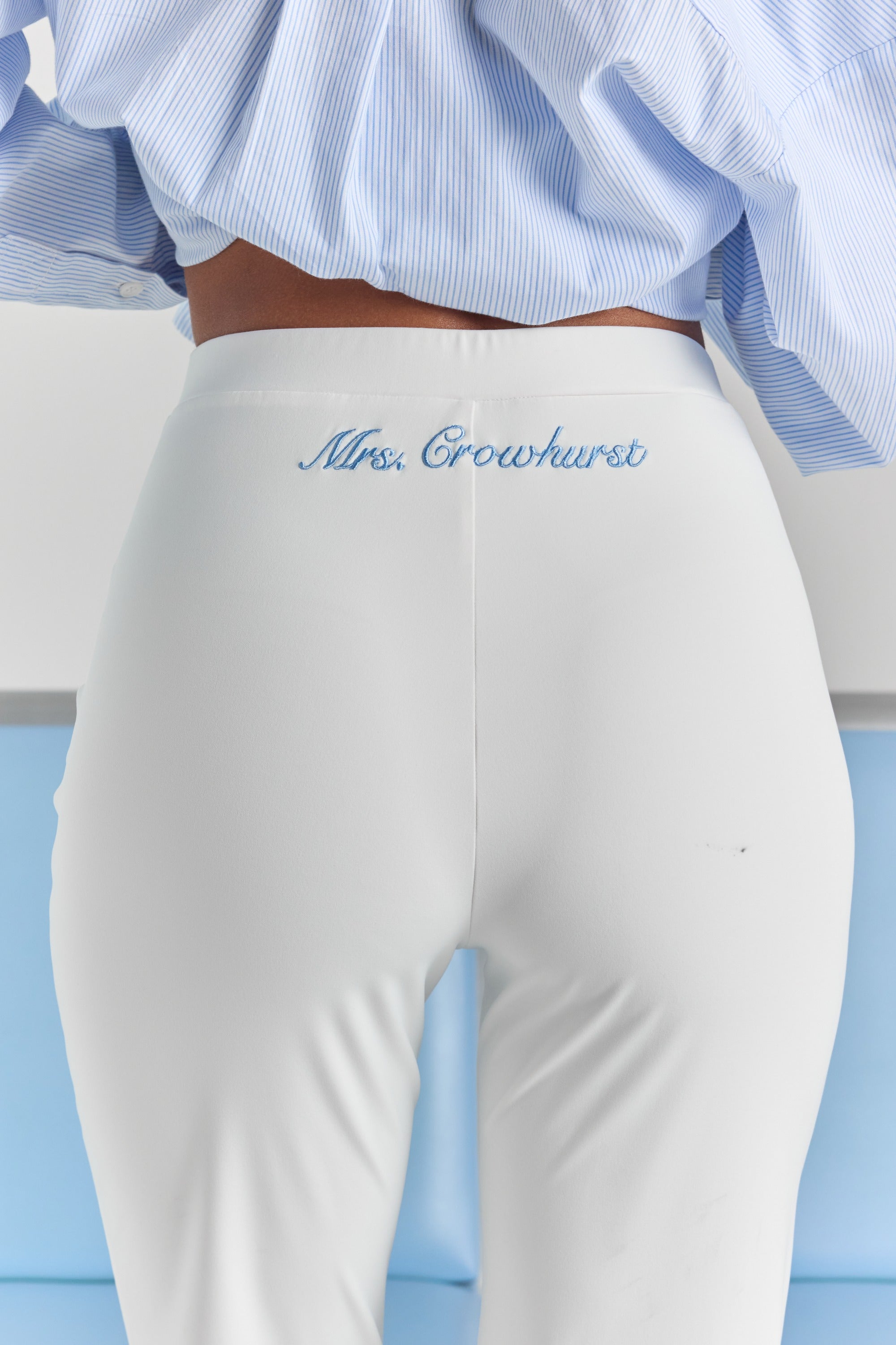 A close-up of personalized embroidery just below the back waistband of the white Vivienne travel pant, centered over the back seam.