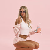 ALT's pink Paris rhinestone velour zip hoodie, shown crouching from the front, worn off the shoulders over a matching tank.