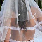 Woman wearing ALT’s Roma top, Margot bottom, Belle Bow veil. a white bridal bikini set, with cacti in the background. White tulle bridal veil with small bow details. Blue embroidery on bottoms Mrs. Kelce