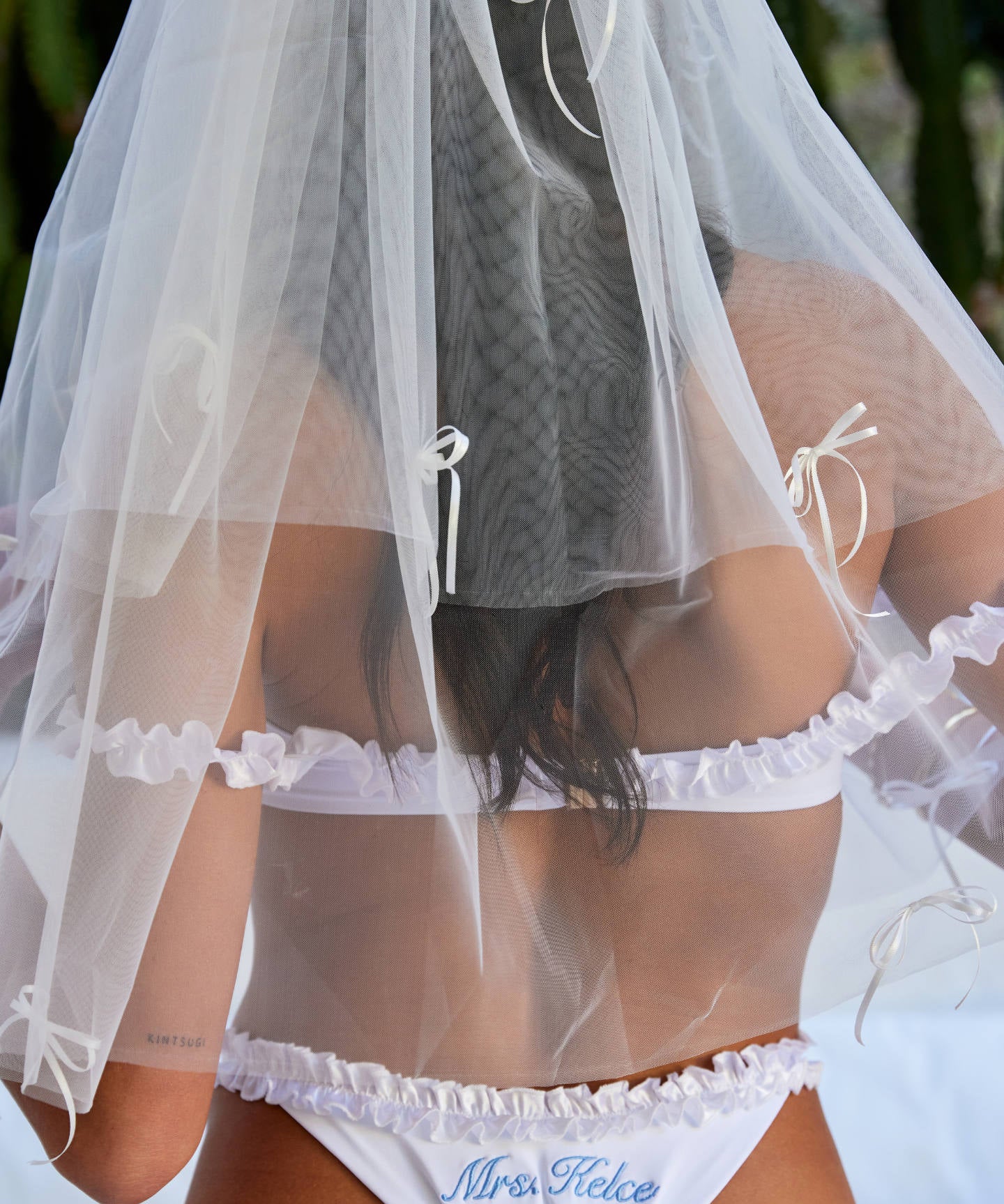Woman wearing ALT’s Roma top, Margot bottom, Belle Bow veil. a white bridal bikini set, with cacti in the background. White tulle bridal veil with small bow details. Blue embroidery on bottoms Mrs. Kelce