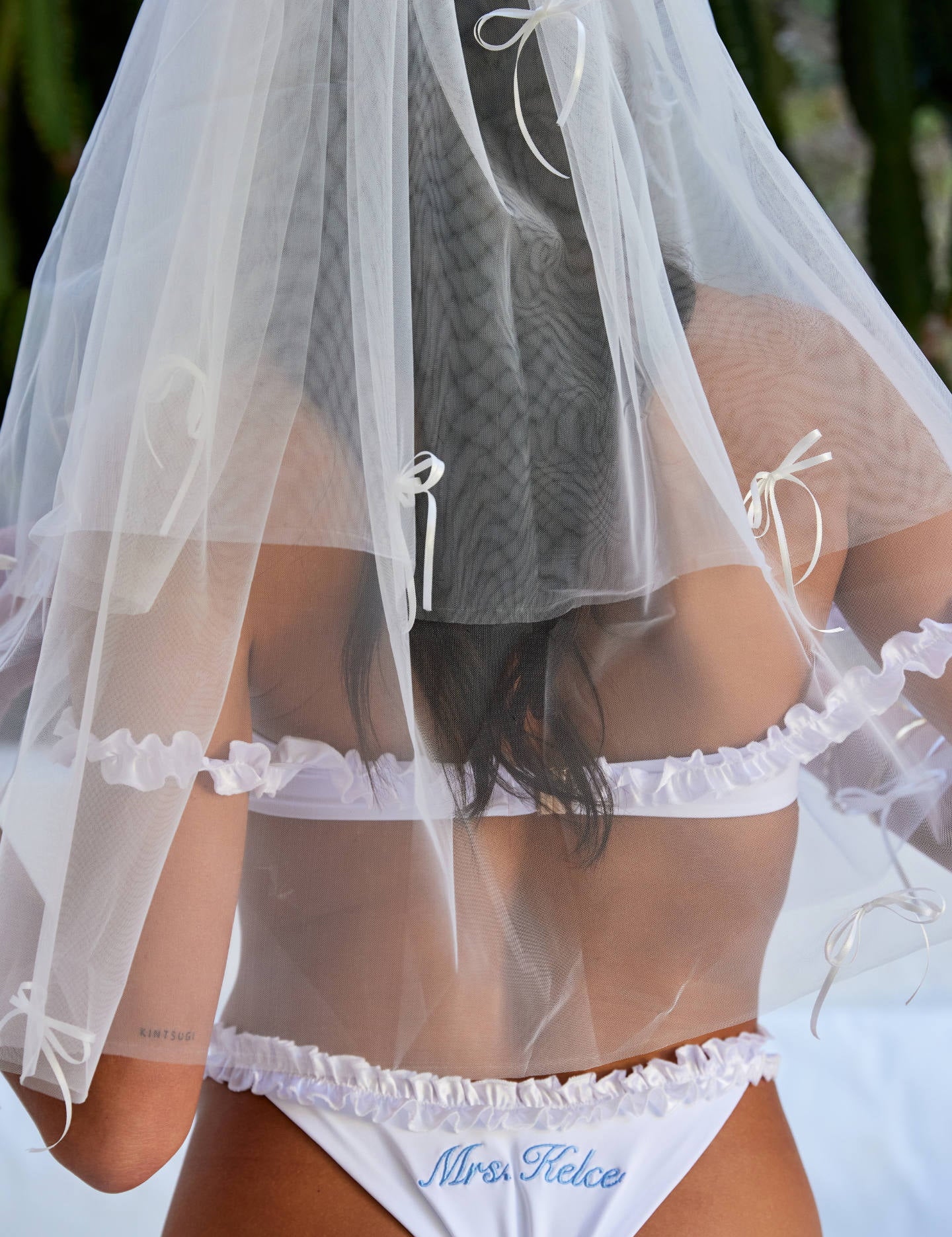 Woman wearing ALT’s Roma top, Margot bottom, Belle Bow veil. a white bridal bikini set, with cacti in the background. White tulle bridal veil with small bow details. Blue embroidery on bottoms Mrs. Kelce