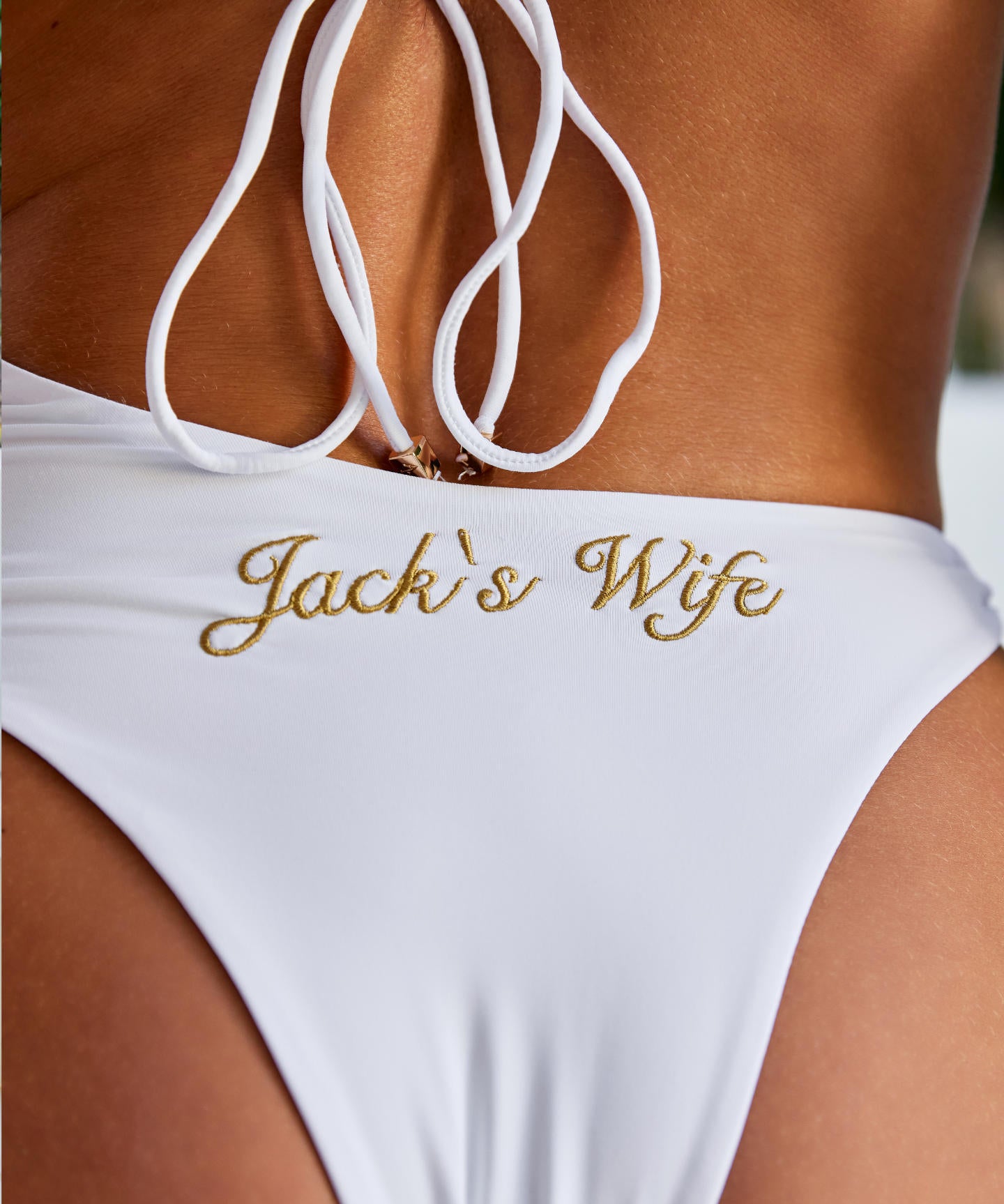 Woman wearing ALT’s Elidy one piece, a white bridal one piece swimsuit with gold chain halter detailing, back tie and gold embroidery Jack's Wife