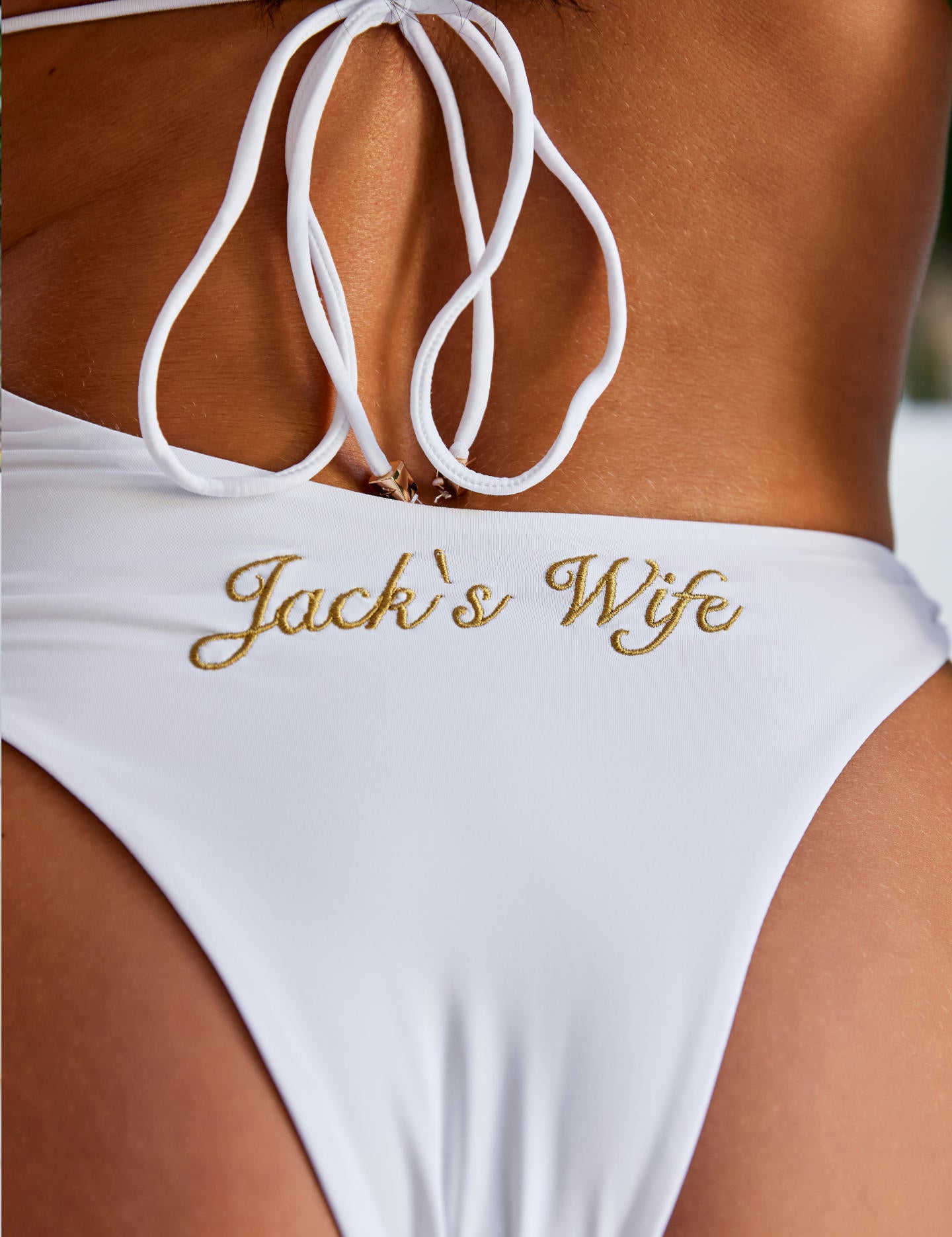 Woman wearing ALT’s Elidy one piece, a white bridal one piece swimsuit with gold chain halter detailing, back tie and gold embroidery Jack's Wife