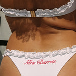 Woman wearing ALT’s Roma top and Margot bottom, a white bridal bikini set, in the streets of st. tropez. Pink embroidery on the back of the bottoms Mrs Barrett