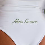 Woman wearing ALT’s Soraya one piece, a white bridal one piece swimsuit, with cacti in the background. ruching and Satin flower detailing Sage green embroidery on the back Mrs. Gomez