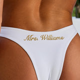 Woman wearing ALT’s Noa top and Talia bottom, a white bridal bikini set, with cacti in the background. Gold and pearl hardware. Gold embroidery Mrs. Williams on the back of bottoms