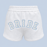 ALT's white Bride Althea track short shown on its own from behind, with BRIDE in blue-outlined varsity applique arched across the back.